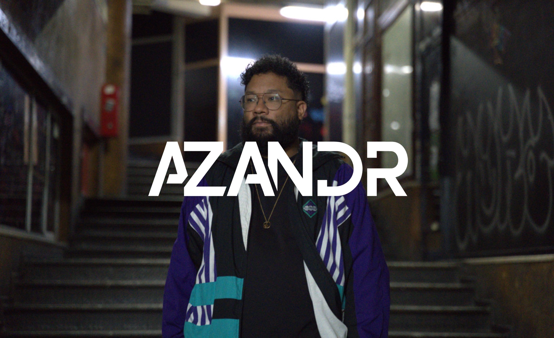 Le logotype Azandr en blanc sur un portrait de l’artiste en veste colorée, dans une cage d’escalier la nuit.