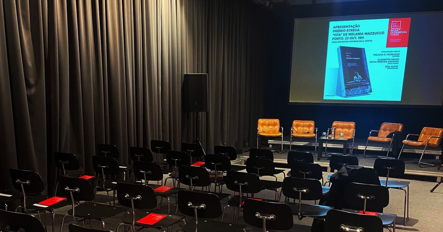 Salle de conférence du Bella Letteratura Forum : rangées de chaises noires marquées d’un carton rouge, écran de projection au fond.
