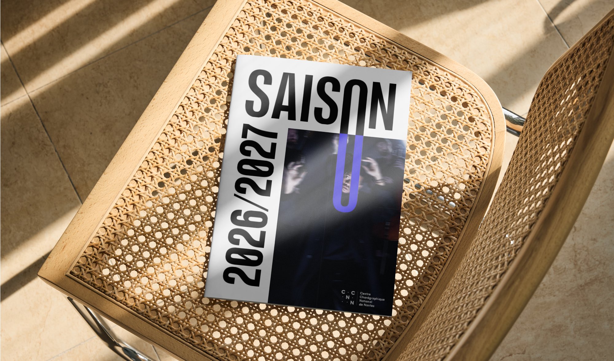 La couverture « Saison 2026/2027 » posée sur l’assise cannée d’une chaise, dans une lumière rasante.