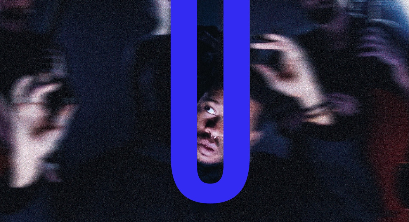 Une foule floue dans la pénombre, mains levées ; seul un visage est net, cerné par un U bleu électrique.