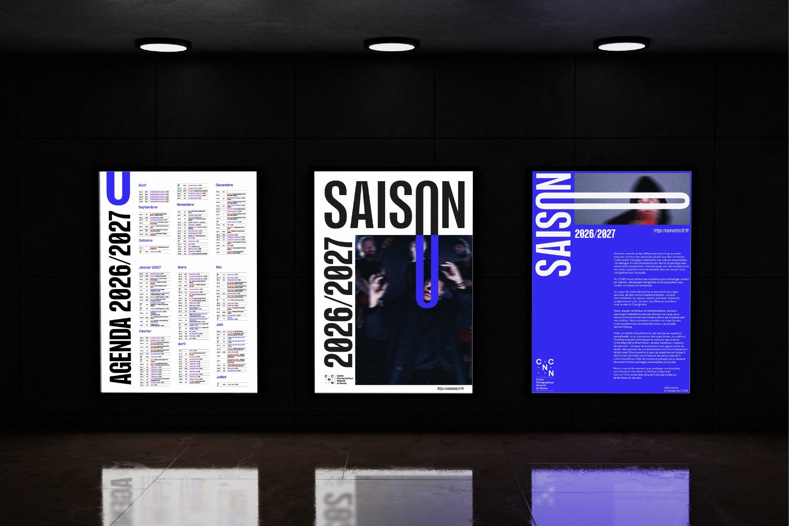 Les trois affiches de la saison éclairées dans des caissons lumineux, sur un mur noir : l’agenda, le visuel annuel et l’édito.