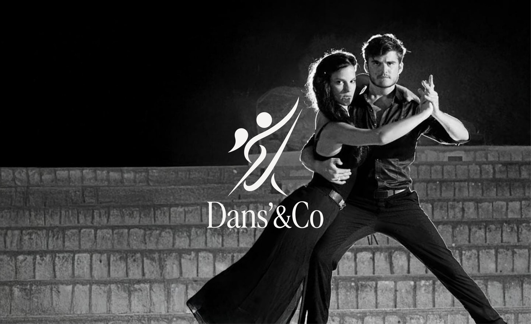 Un couple en position de tango devant un mur de briques, le symbole du studio au premier plan.
