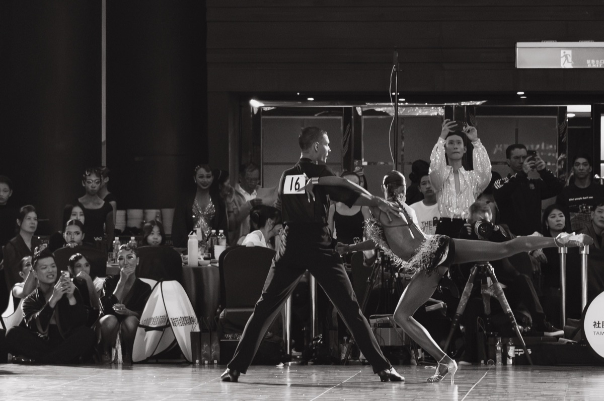Un couple de danse latine en pleine figure devant le public d'un concours.