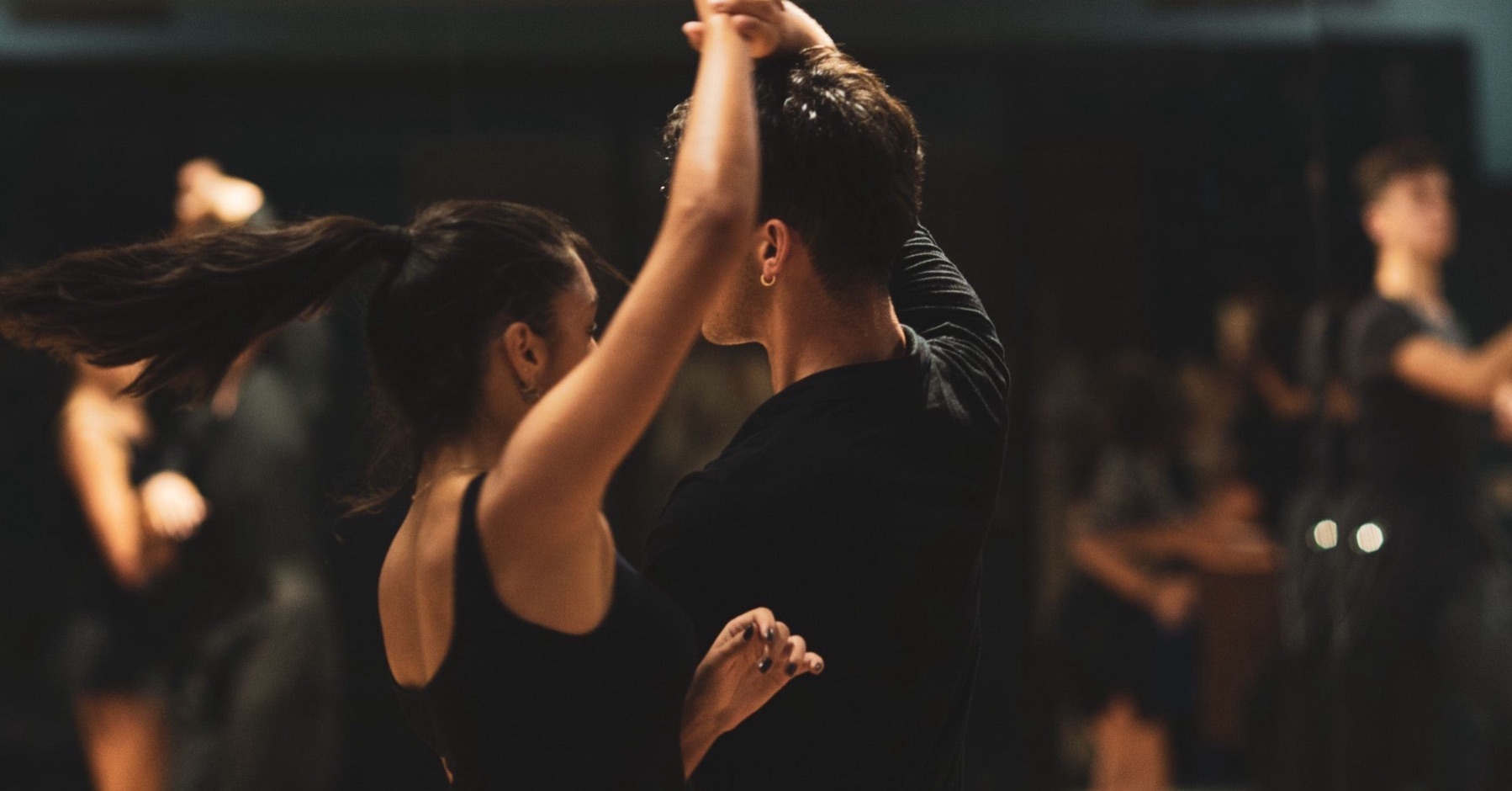 Un couple de danseurs bras levés dans un studio, les autres élèves en arrière-plan.