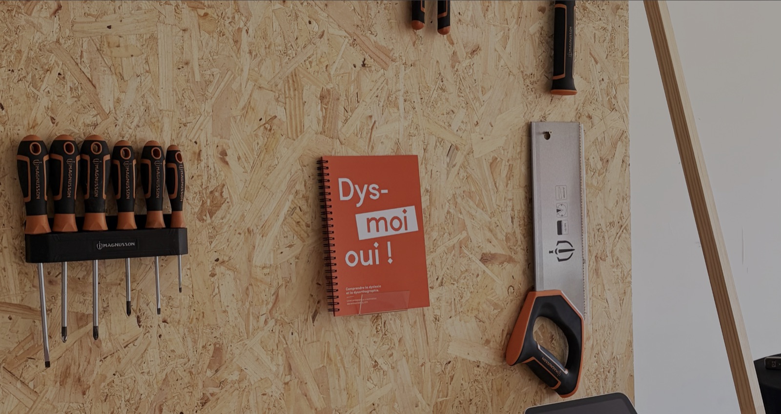 Le livret orange accroché au mur de l’atelier, entre un porte-tournevis et une scie.