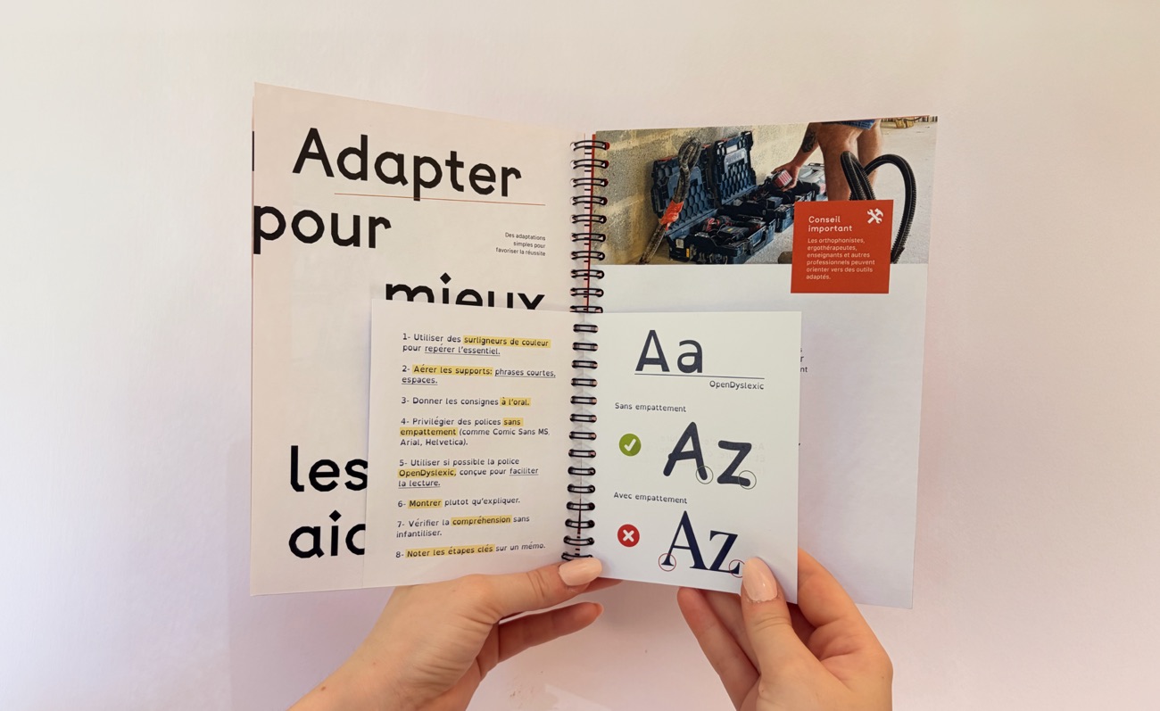 Deux mains tenant le livret ouvert sur la fiche typographique « Aa / Az », devant la double page « Adapter pour mieux les aider ».