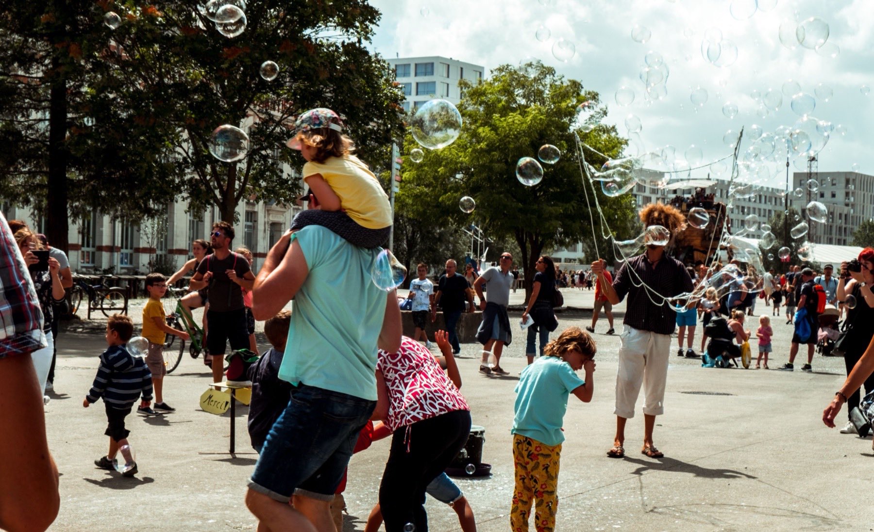 Des bulles de savon au-dessus de la place, un enfant sur les épaules de son père.
