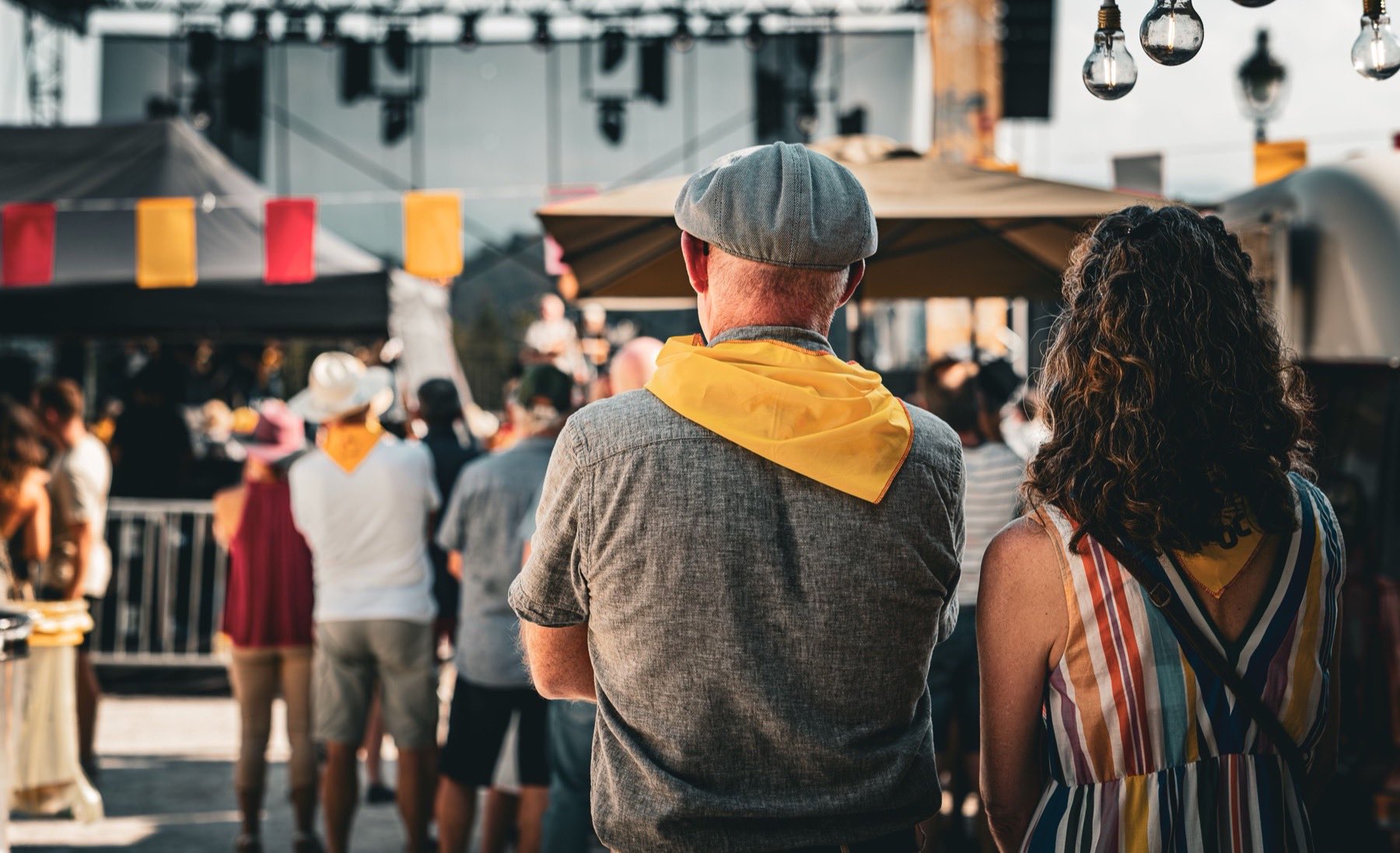 Deux festivaliers de dos devant la scène, des fanions colorés au-dessus de la foule.