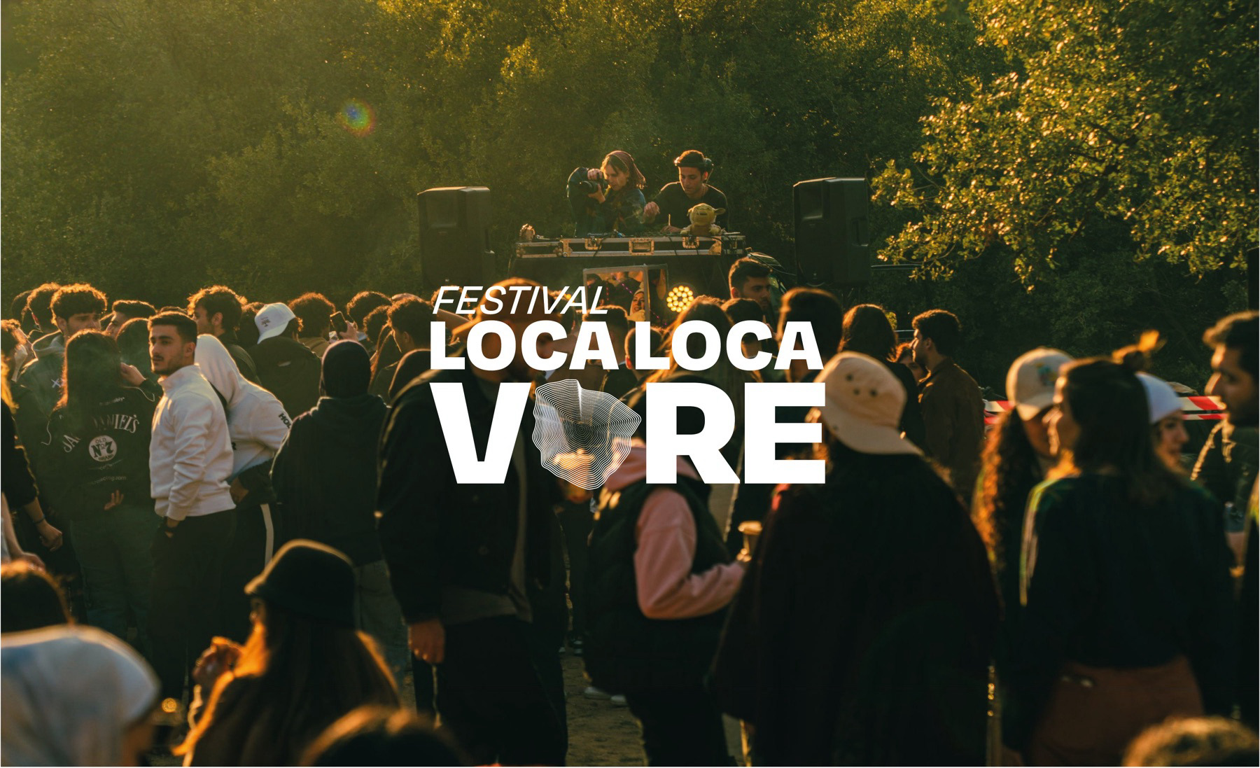 La foule du festival au coucher du soleil devant la scène, le logotype en filigrane blanc.