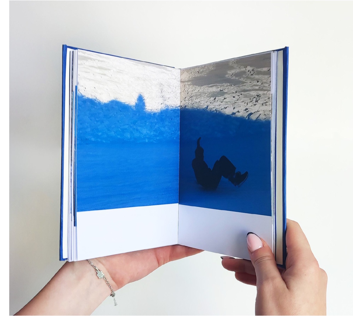 Double page : une vague bleue en pleine largeur, une silhouette en ombre chinoise sur la page de droite.